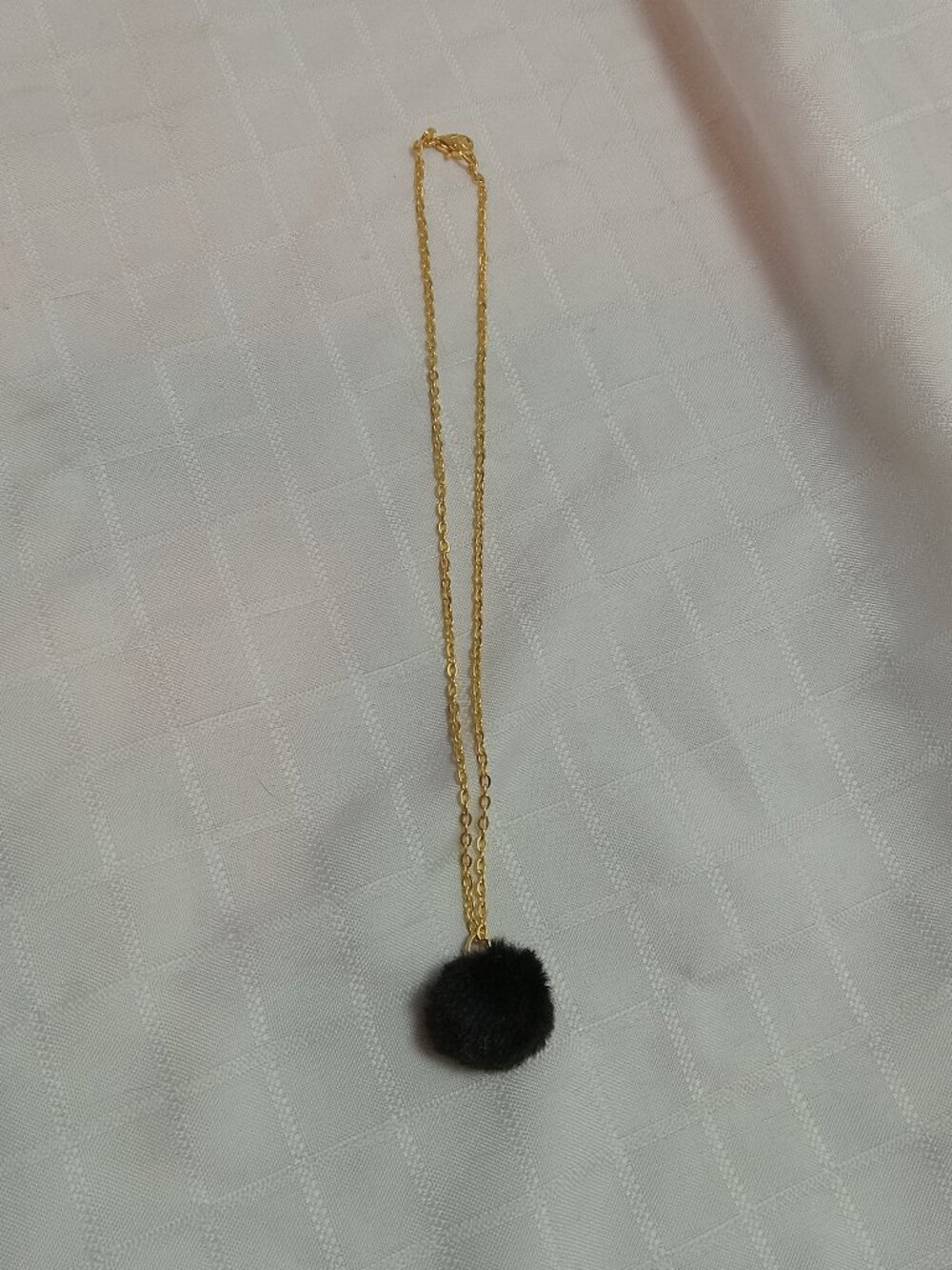 Handmade necklace with a small pom-pom and gold-colored accent hooks and chains